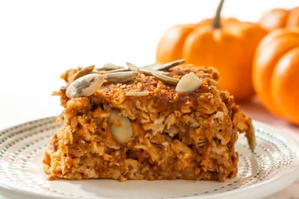 a sliced of baked pumpkin oatmeal with pumpkin seeds on top and mini pumpkins in the background