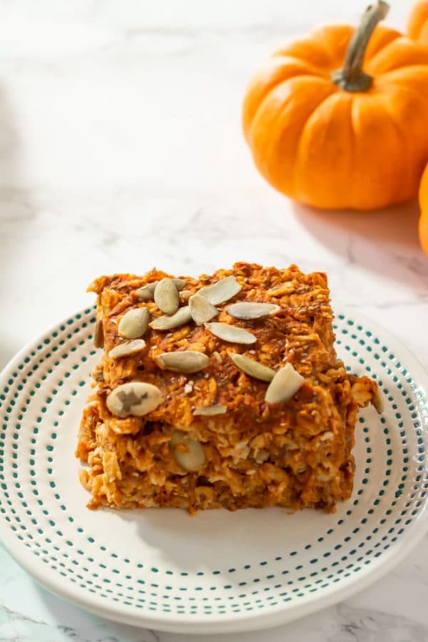 A square of baked pumpkin oatmeal topped with pepitas on a small ivory plate with tiny teal dots on the border.