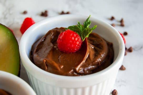 Close up of creamy chocolate raspberry avocado pudding in a white ramekin garnished with a sprig of mint and a fresh raspberry.