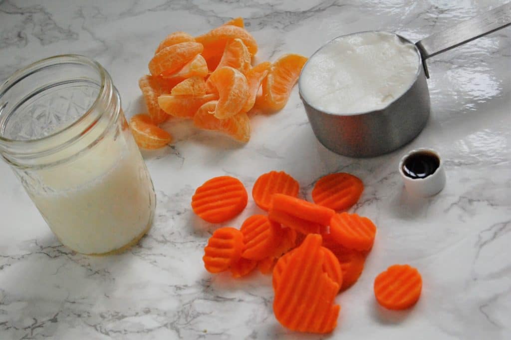 Ingredients for the creamsicle clementine smoothie laid out: clementines, carrots, milk, vanilla greek yogurt, and vanilla extract