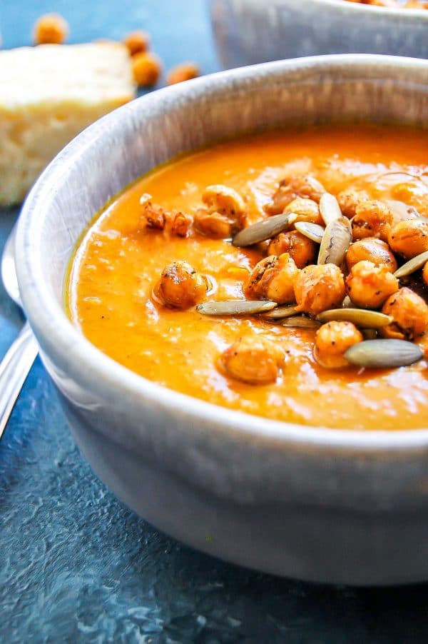 A close-up of spiced sweet potato carrot soup in a handmade gray ceramic bowl on a blue board.