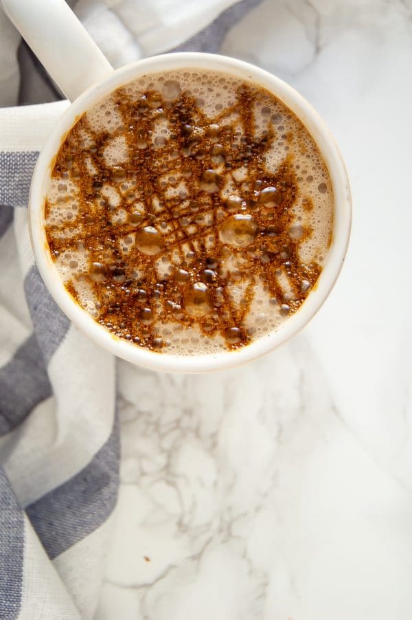 A warm ivory mug with a cozy gingerbread chai latte with molasses drizzle on top.