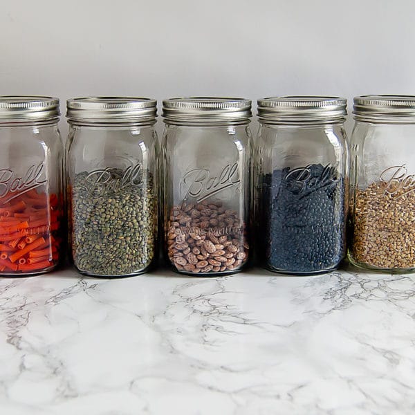 Wide-mouth mason jars full of dried legumes, grains, and lentil pasta.