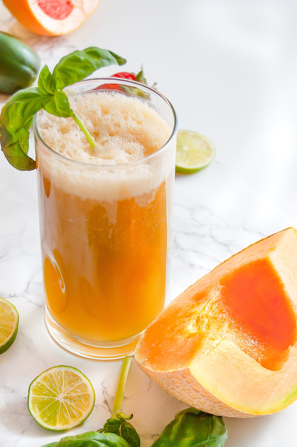 Tall glass of cantaloupe basil agua fresca next to a slice of cantaloupe.