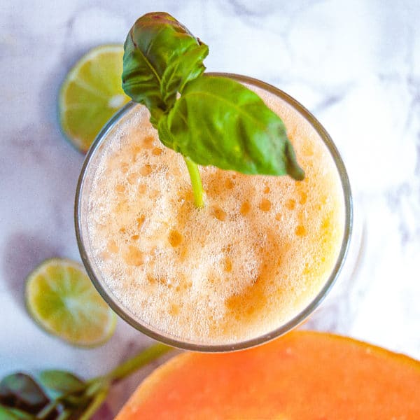 Overhead picture of a glass of cantaloupe basil agua fresca with a pretty soft orange froth and basil garnish.