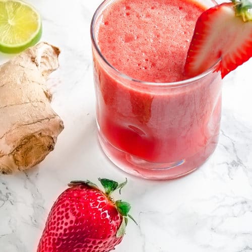 Strawberry ginger agua fresca surrouned by fresh strawberries, lime, and ginger.