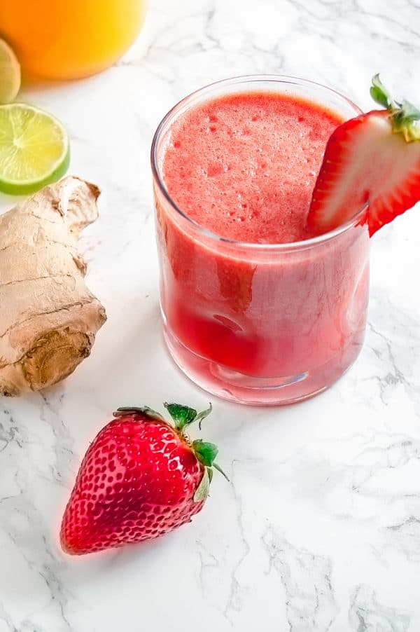 Strawberry ginger agua fresca surrouned by fresh strawberries, lime, and ginger.