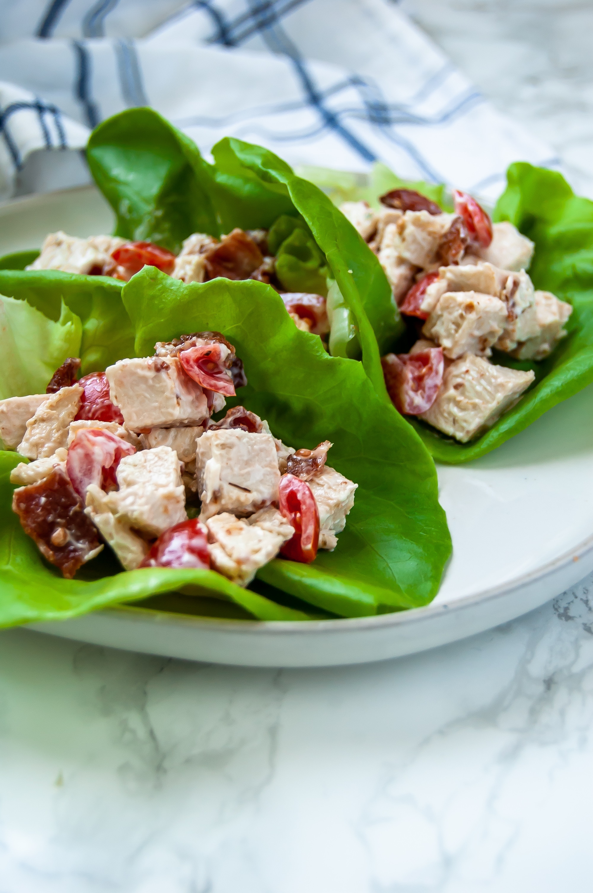 A plate with turkey lettuce BLT cups on it - there are three leaves of butter lettuce with a creamy turkey, bacon, tomato salad inside of them.