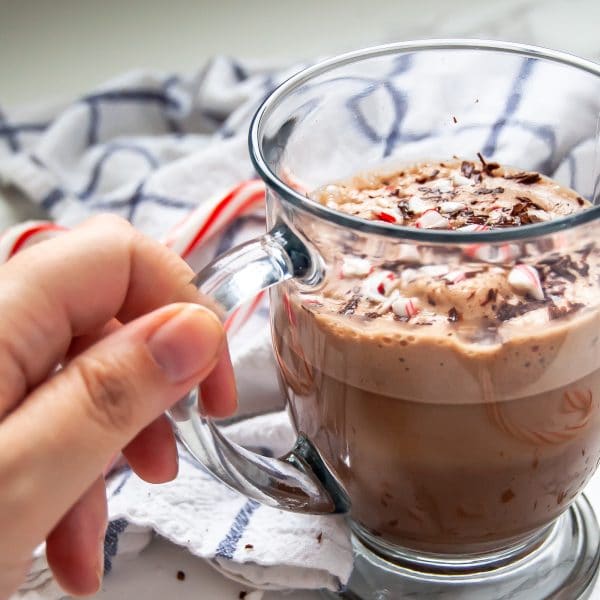 A hand holding a glass mug of peppermint hot chocolate.