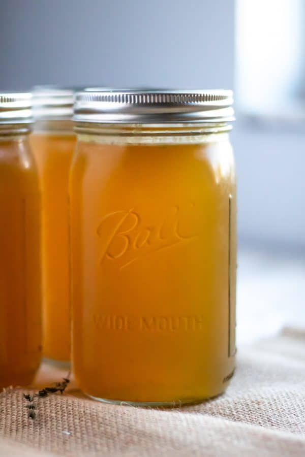 3 tall ball jars full to the brim with homemade slow cooker turkey stock with light coming in from a window in the background.