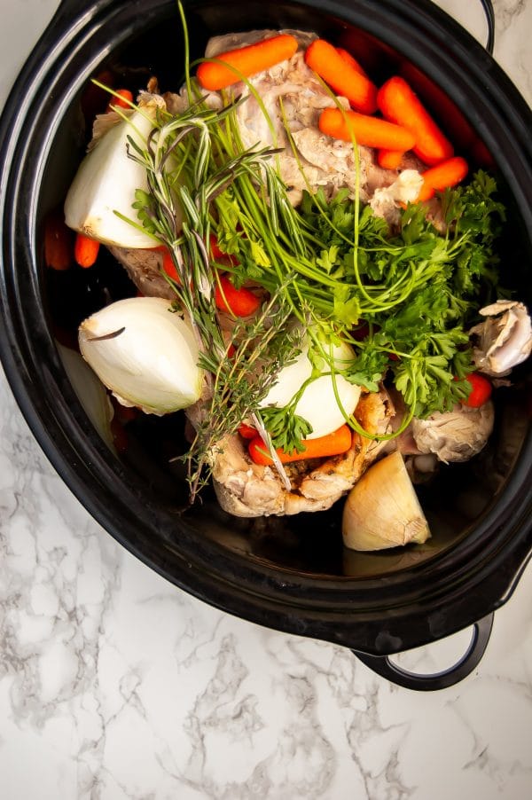 A slow cooker filled with the fresh ingredients for the easiest slow cooker turkey stock recipe.