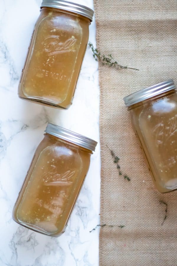 3 ball jars of homemade slow cooker turkey stock placed on marble and burlap with fresh thyme.