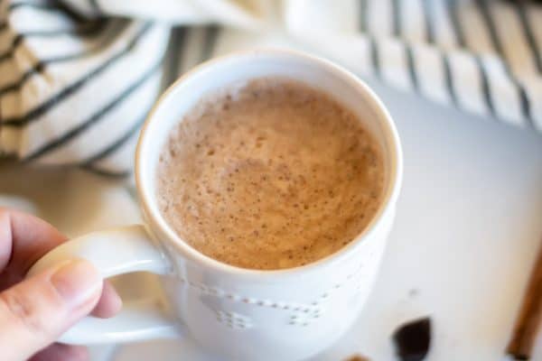 A hand holding a cozy white mug of chocolate chai tea.