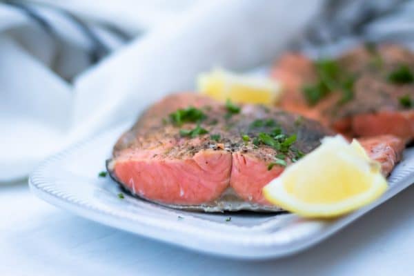 Close up of beautifully cooked salmon fillets with lemon wedges and fresh parsley on a white platter.