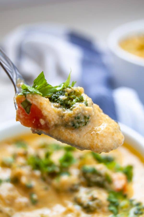 A spoonful of vegan broccoli cheese soup hovers above a white bowl of soup.