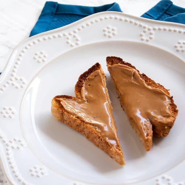 a piece of whole grain toast with peanut butter on a white plate, sliced on the diagonal