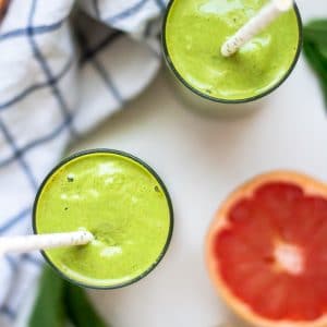 Long image looking down overhead at two green grapefruit smoothies with ingredients on the side.