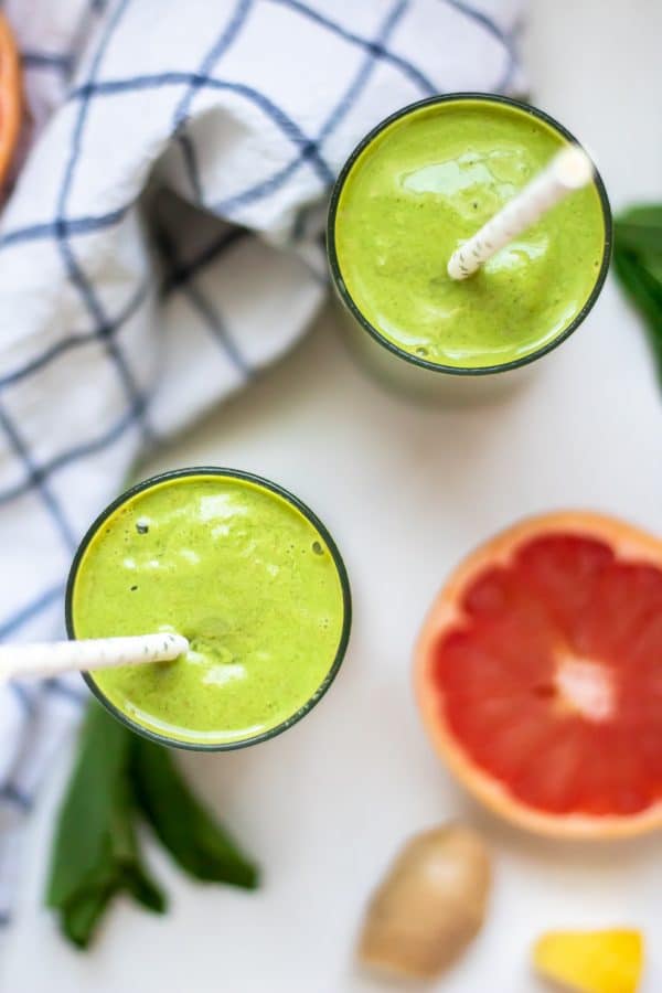 Long image looking down overhead at two green grapefruit smoothies with ingredients on the side.