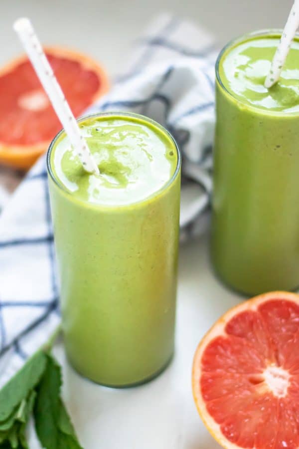 Tall thin glasses of green grapefruit smoothies with pink grapefruits and fresh mint on the side.