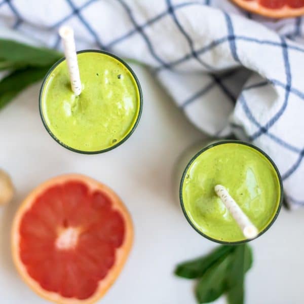 A square, overhead shot looking down at two green grapefruit smoothies with paper straws.