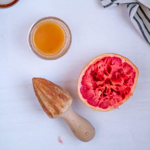 A handheld citrus juice, half a juiced grapefruit, and a small mason jar with the ingredients of a simple grapefruit vinaigrette.