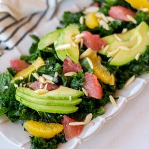 Rectangular plate full of a citrus kale salad massaged with grapefruit vinaigrette and topped with sliced avocado, citrus segments, and slivered almonds.