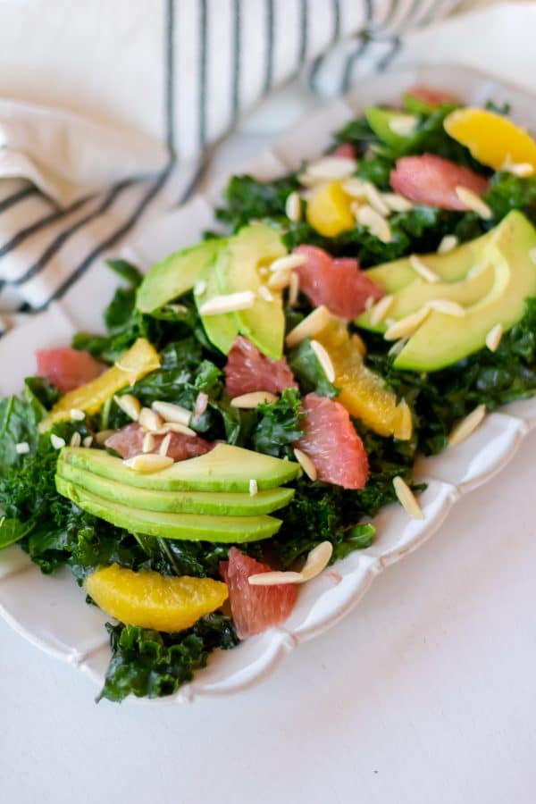 Rectangular plate full of a citrus kale salad massaged with grapefruit vinaigrette and topped with sliced avocado, citrus segments, and slivered almonds.