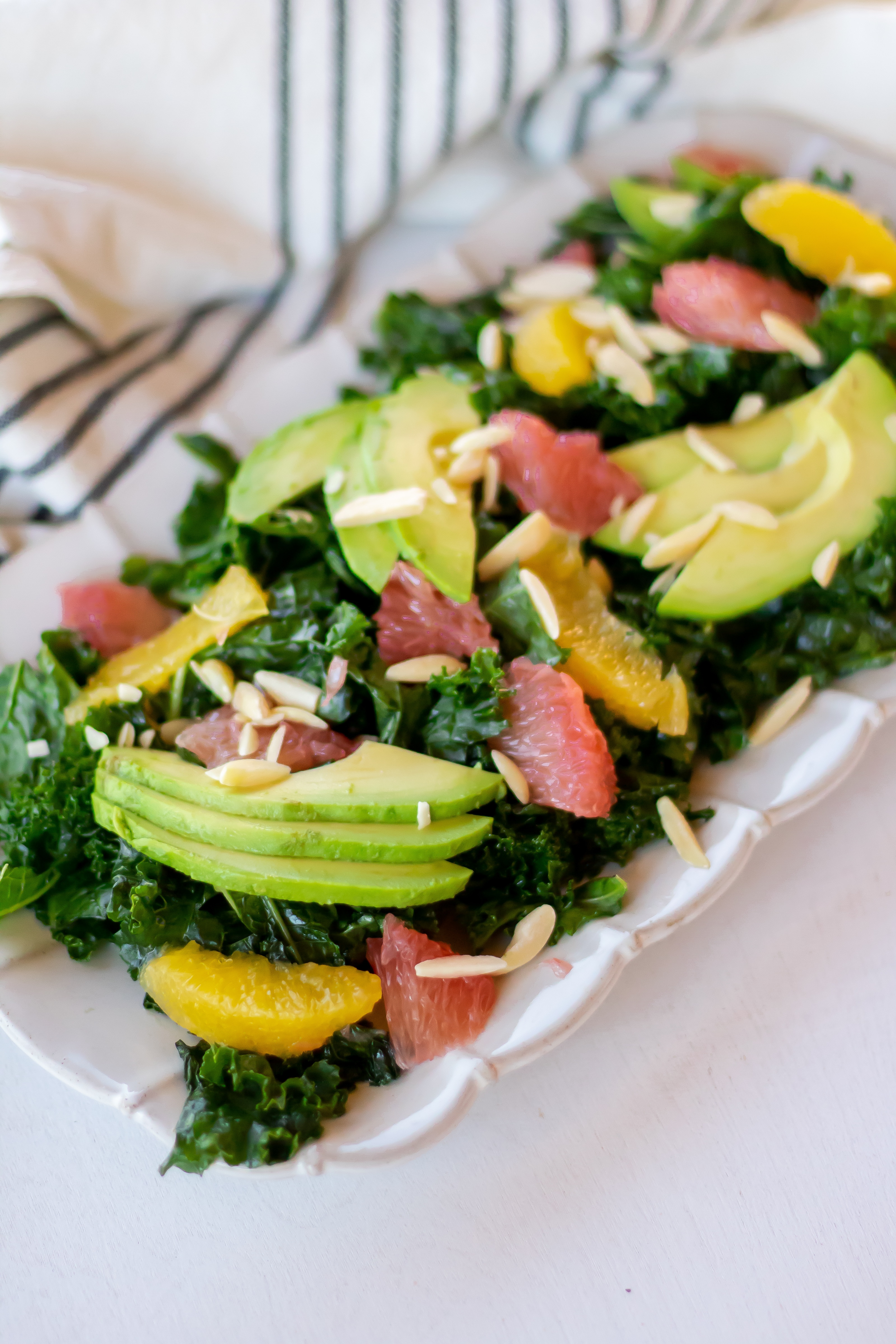 Rectangular plate full of a citrus kale salad massaged with grapefruit vinaigrette and topped with sliced avocado, citrus segments, and slivered almonds.