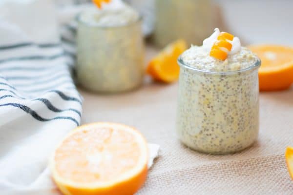3 small glasses of orange chia pudding with collagen on a burlap table runner with orange slices. Garnished with coconut whipped cream and curled orange peel garnishes.