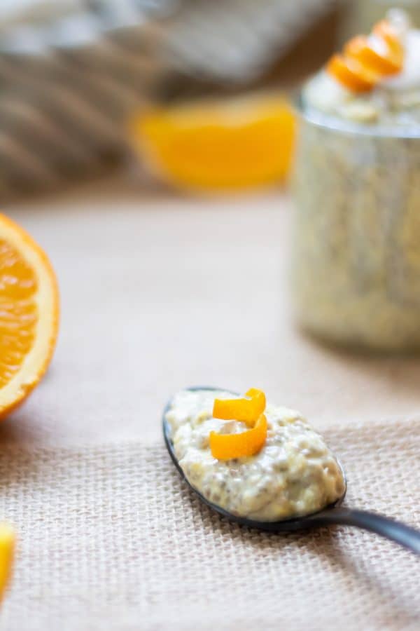 A spoonful of orange chia pudding on a black spoon with a curl of orange peel on top.