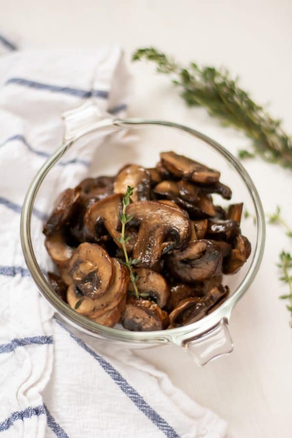 Overhead shot of healthy, easy sauteed mushrooms in a glass bowl garnished with a sprig of thyme.