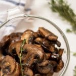 funghi sani e facili saltati in una ciotola di vetro guarniti con un rametto di timo.