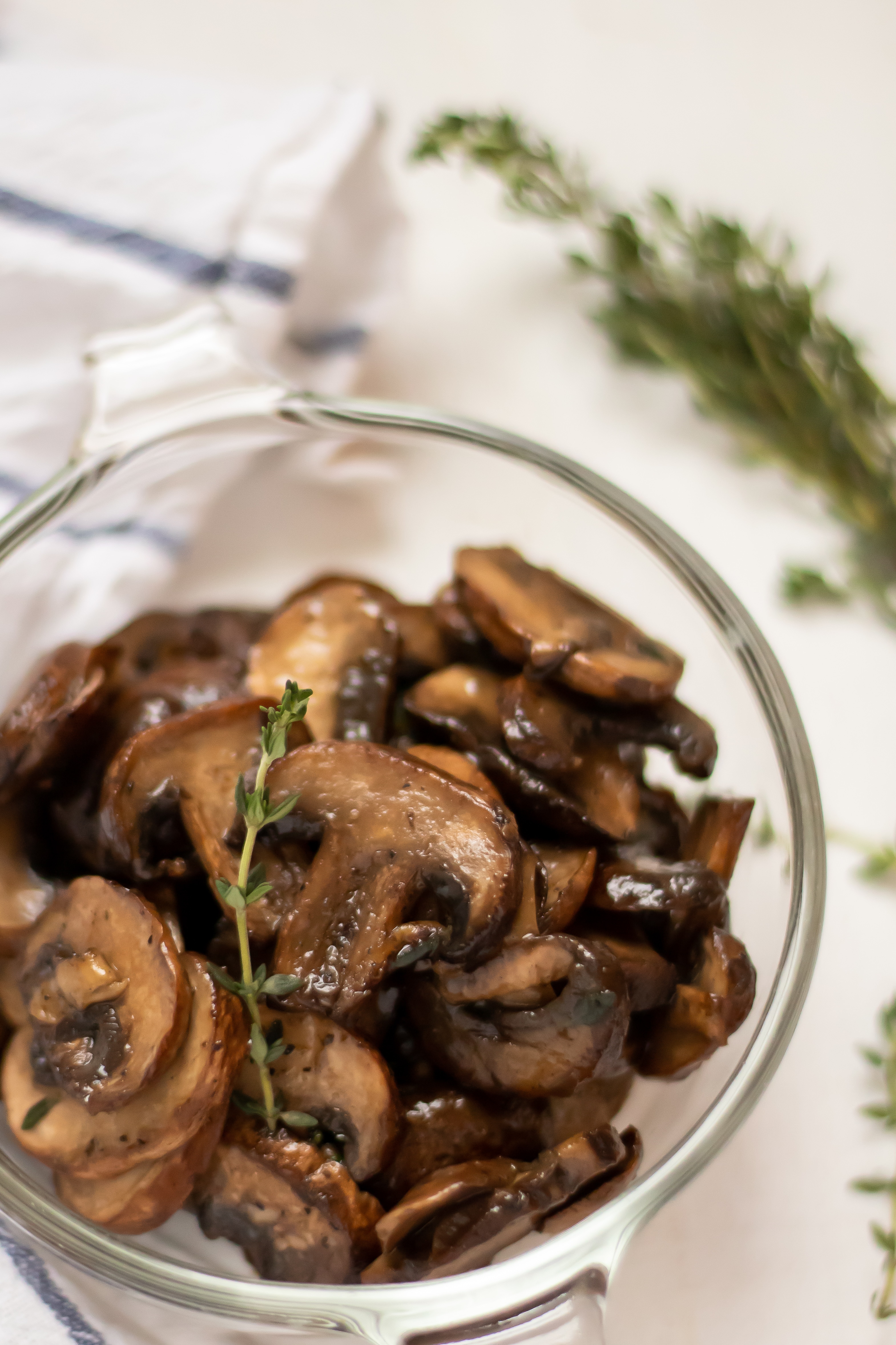 healthy, easy sauteed mushrooms in a glass bowl garnished with a sprig of thyme.