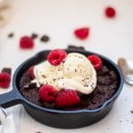 Skillet brownies with raspberries in a six inch skillet topped with vanilla bean ice cream and fresh raspberries.