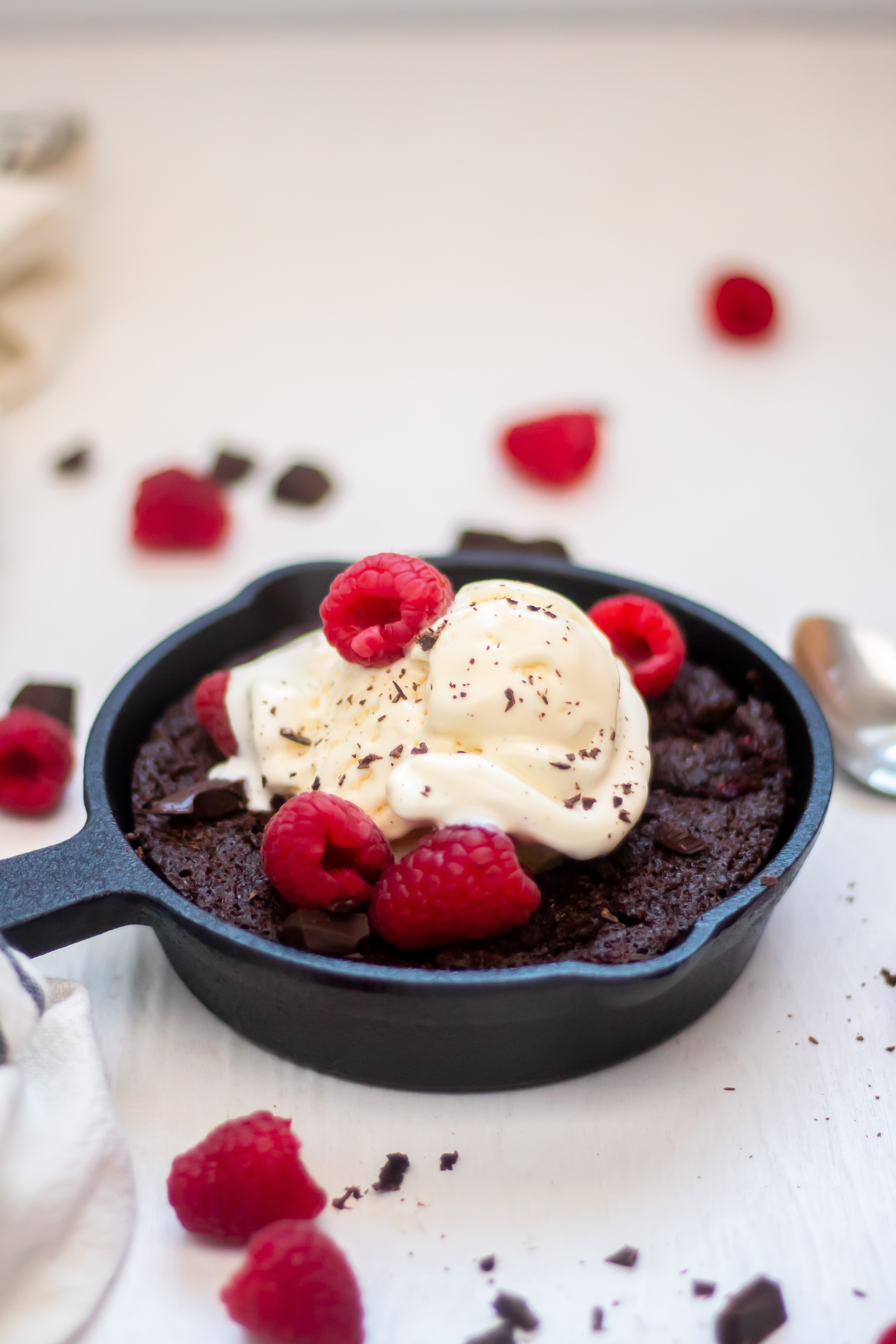 Skillet brownies with raspberries in a six inch skillet topped with vanilla bean ice cream and fresh raspberries.