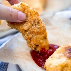 A garlic parmesan chicken tender being dipped in ketchup.