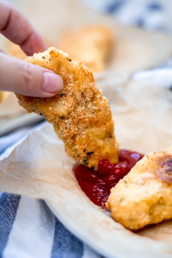 A garlic parmesan chicken tender being dipped in ketchup.