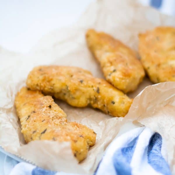 Garlic parmesan chicken tenders in natural parchment paper on a blue striped linen towel.