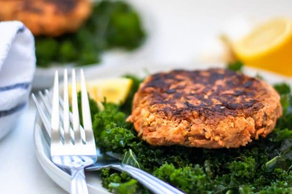 A salmon patty on a massaged kale salad with lemons on the side.