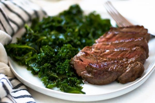 Horizontal image of sliced cast iron skillet steak next to massaged kale salad.