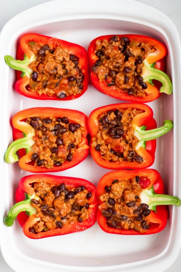 Red bell peppers stuffed with turkey filling for taco stuffed peppers in a white casserole dish.