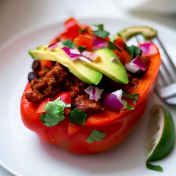 A close up of a taco stuffed pepper with fresh taco toppings like avocado, red onion, and cilantro.