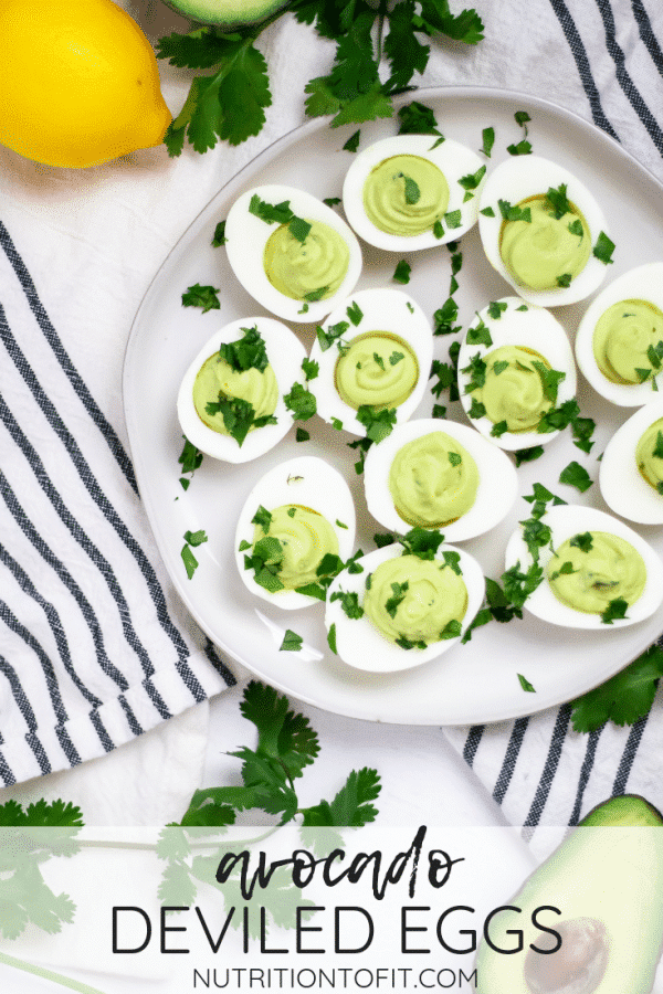 Plate with avocado deviled eggs garnished with cilantro on a black and cream striped kitchen towel.