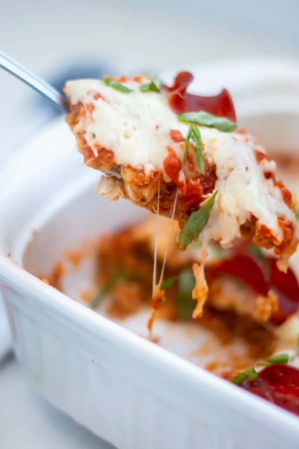 A spoon scooping out a serving of pizza quinoa casserole with gooey melty cheese on top and fresh basil.