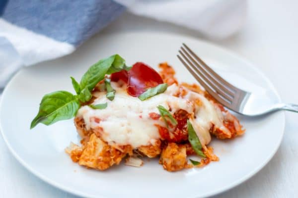 A serving of pizza quinoa casserole on a white plate with gooey cheese, turkey pepperoni, and fresh basil.