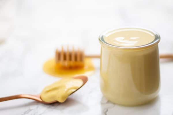 Glass jar of healthy honey mustard salad dressing with a honey wand and spoon of mustard next to it.