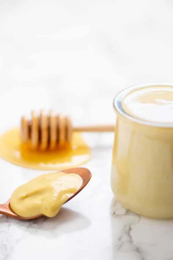 Glass jar of healthy honey mustard salad dressing on a marble surface.