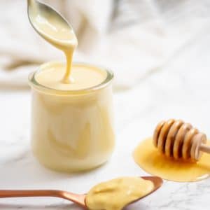 A spoon drizzling healthy honey mustard dressing back into a glass jar of dressing.