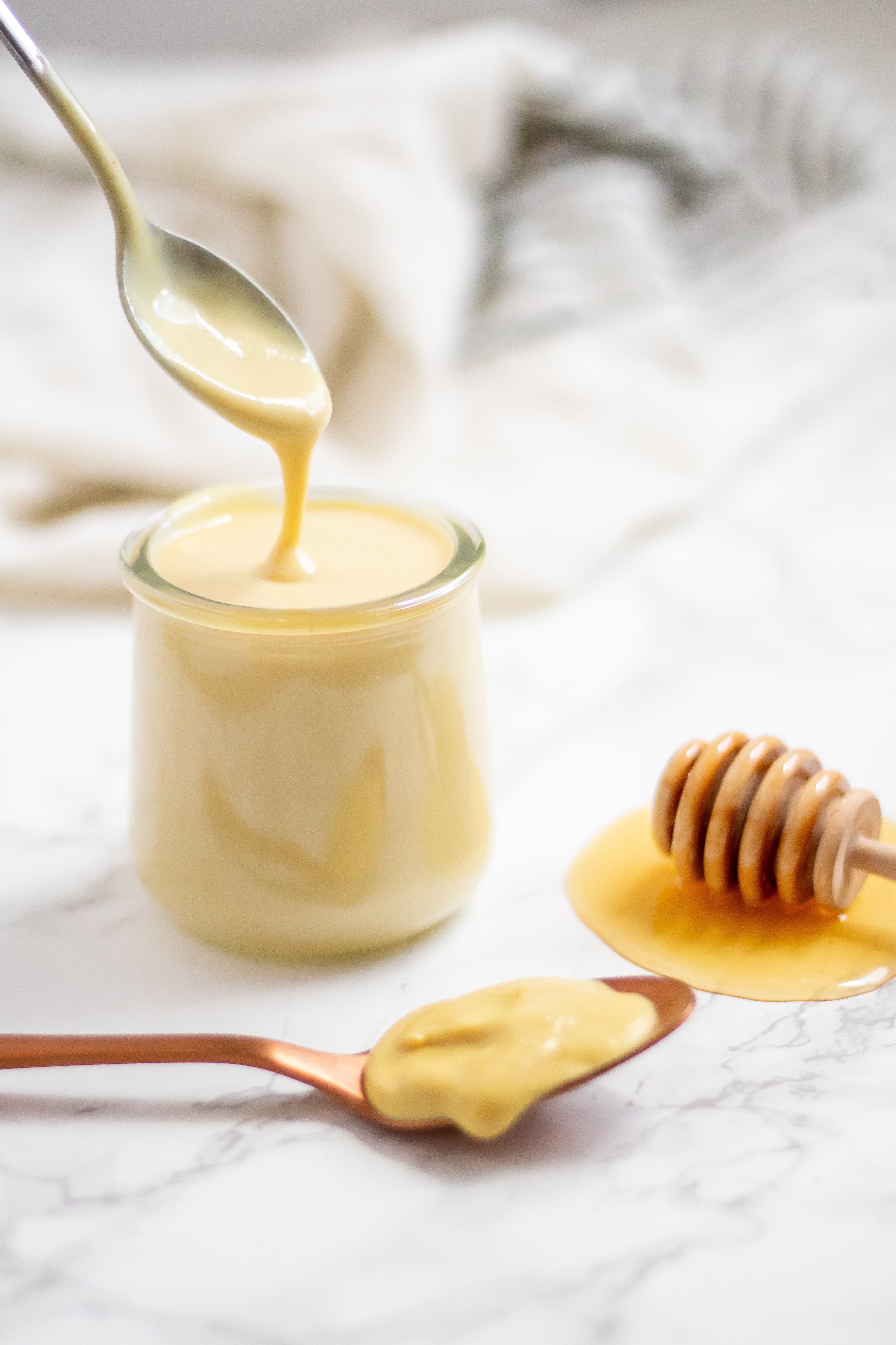 A spoon drizzling healthy honey mustard dressing back into a glass jar of dressing.