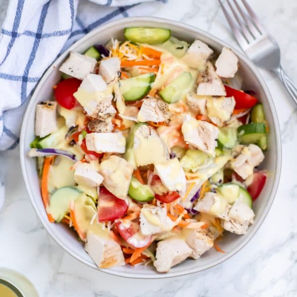 An overhead shot of a grilled chicken salad drizzled with healthier honey mustard salad dressing.